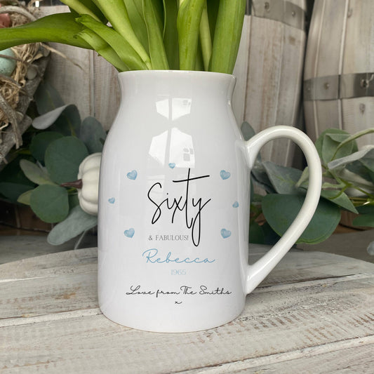 Personalised ceramic jug with 'Sixty & Fabulous' design, blue heart accents, and custom name and message, used as a vase for flowers