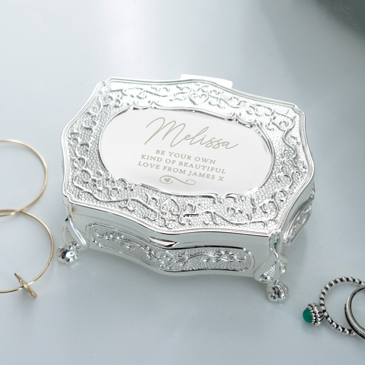 Decorative silver jewellery box with engraved text on a light gray background