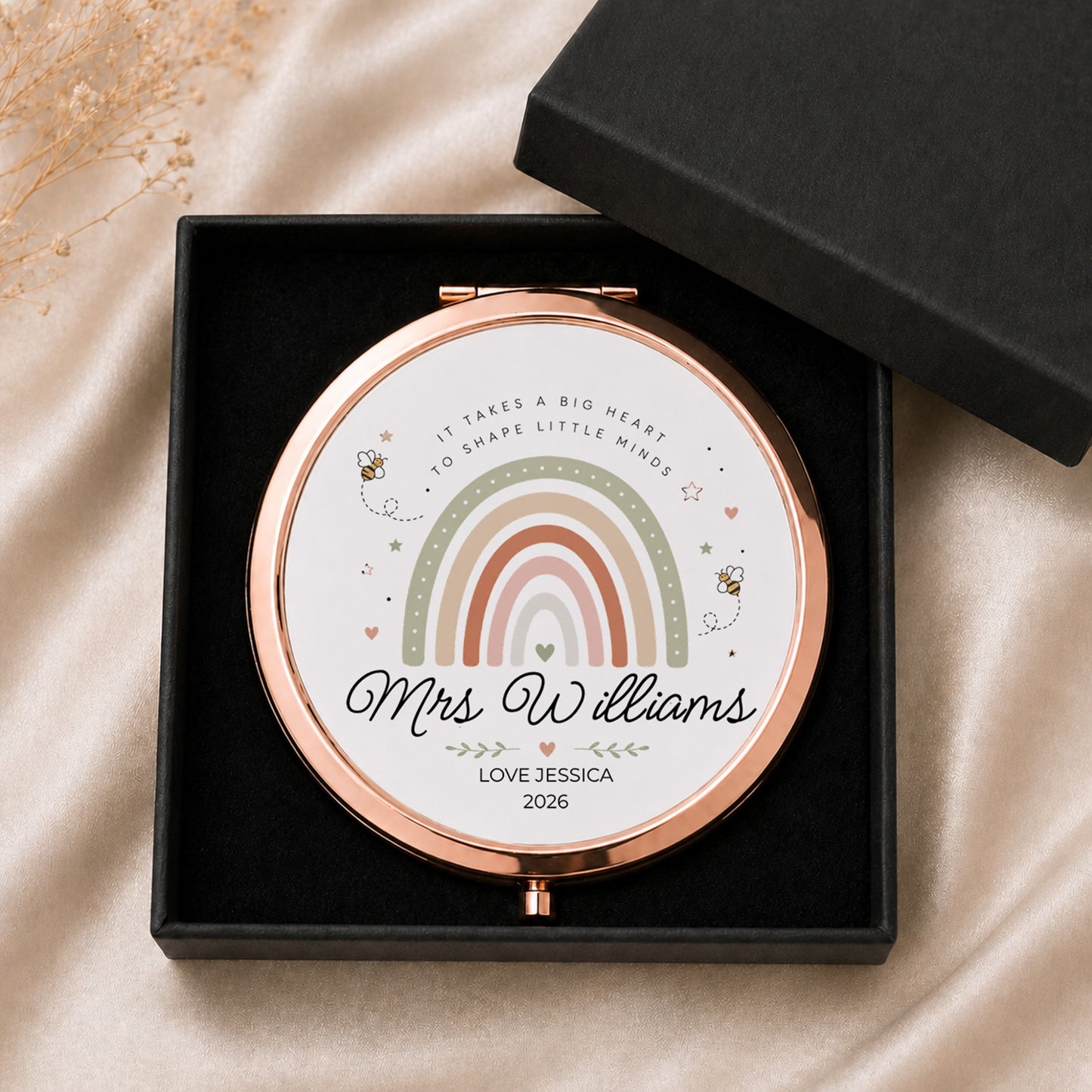 Personalized teacher compact mirror with rainbow design and text in a black box on a beige fabric background