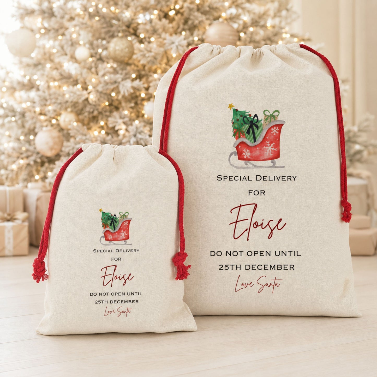 Two personalized Christmas gift bags in natural canvas with red drawstrings, featuring a red sleigh illustration and custom text, displayed in front of a blurred decorated Christmas tree.