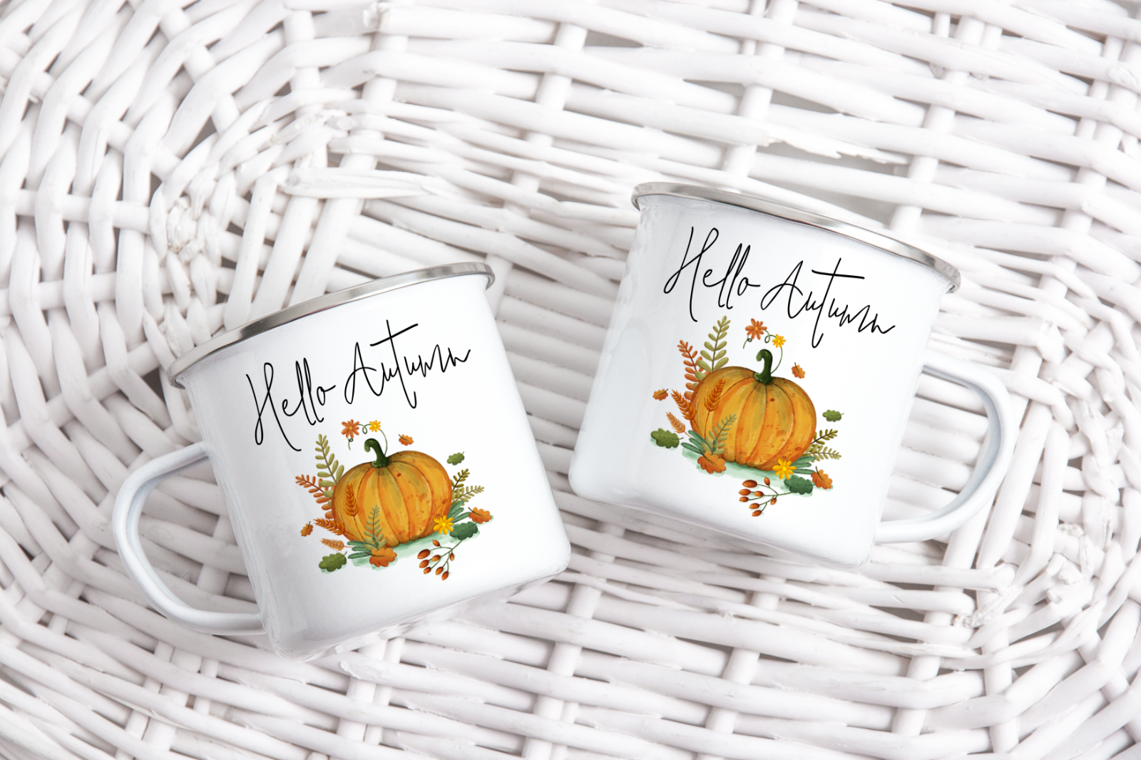 Two white mugs with 'Hello Autumn' text and pumpkin graphics on a wicker surface.