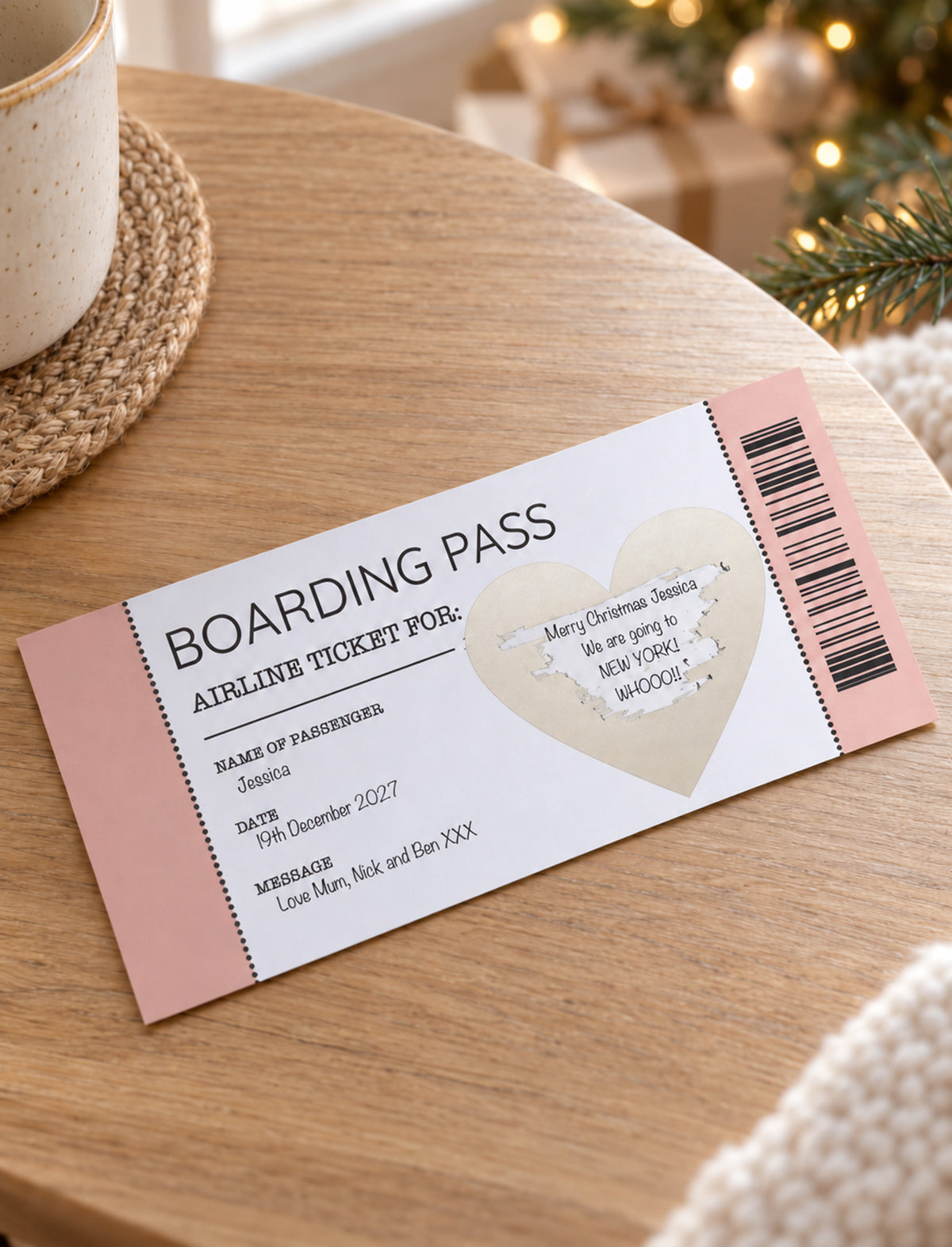 A printed boarding pass styled like an airline ticket, shown on a wooden tabletop with a mug, wrapped gifts, and holiday lights in the background. The ticket is white with pink side panels, black text, a barcode, and a heart-shaped ticket stub area.