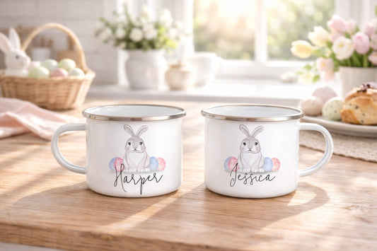 Two mugs with bunny designs and names on a wooden table with Easter decor.