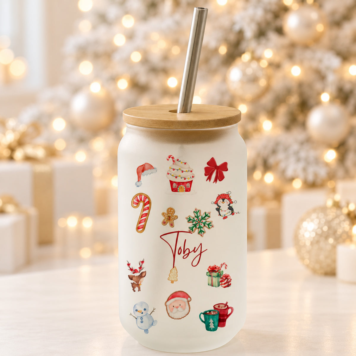 A frosted white Christmas-themed tumbler with a bamboo lid and stainless steel straw. The cup is decorated with various festive illustrations including Santa Claus, a candy cane, a penguin, a snowman, and the name 'Juby' in red script.