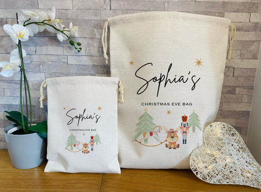 Two Christmas eve themed bags with personalised names printed on them, one larger and one smaller, against a wooden surface with decorative elements.