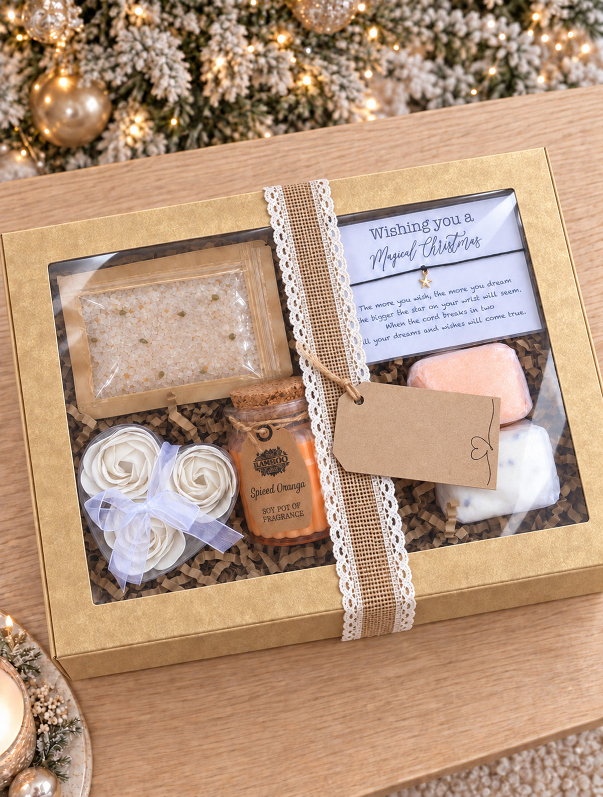 A Christmas-themed gift box set on a wooden table, fAn open Secret Santa gift box filled with spa and self-care items on a wooden surface, including a candle jar, two shower steamers, a packet of bath salts, rolled bath soap, and a handwritten gift message card.