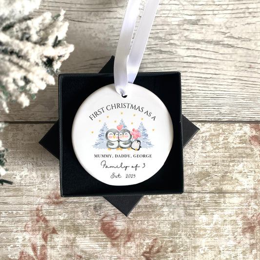 Personalised First Christmas as a Family of 3 ornament with penguins in a black box on a rustic wooden surface.