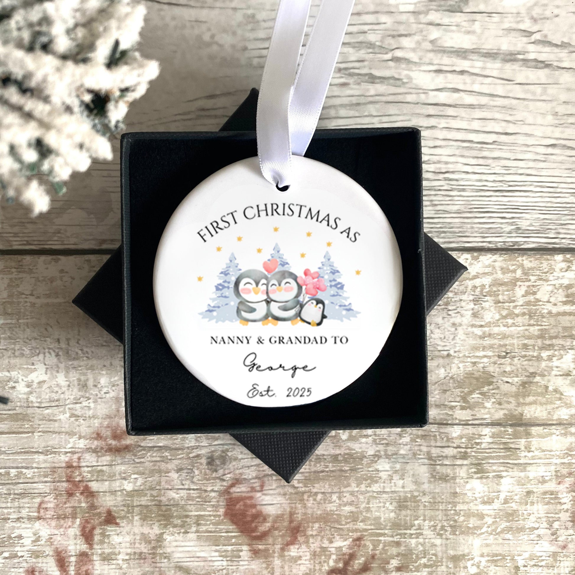 Personalised Christmas ornament with text and design, placed in a black box on a wooden surface.
