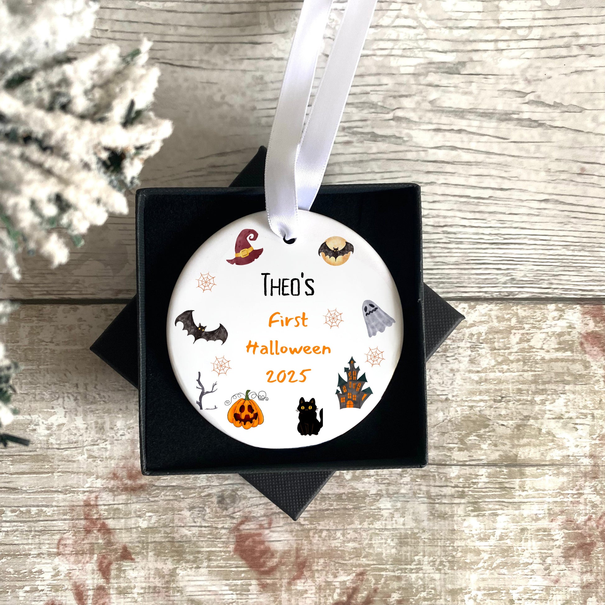 Decorative ornament for 'Theo's First Halloween 2025' with Halloween-themed illustrations on a wooden surface.