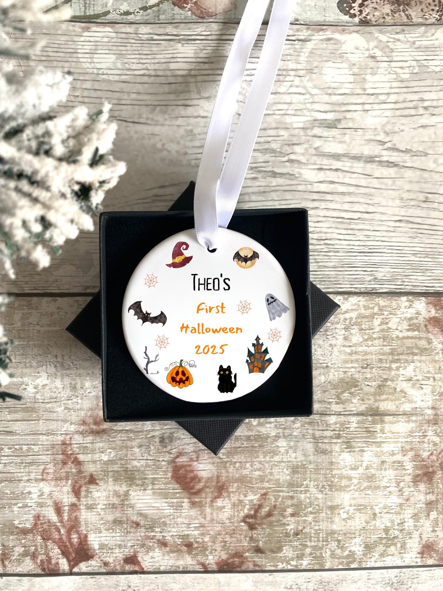 Decorative ornament for 'Theo's First Halloween 2025' with Halloween-themed illustrations on a wooden surface.