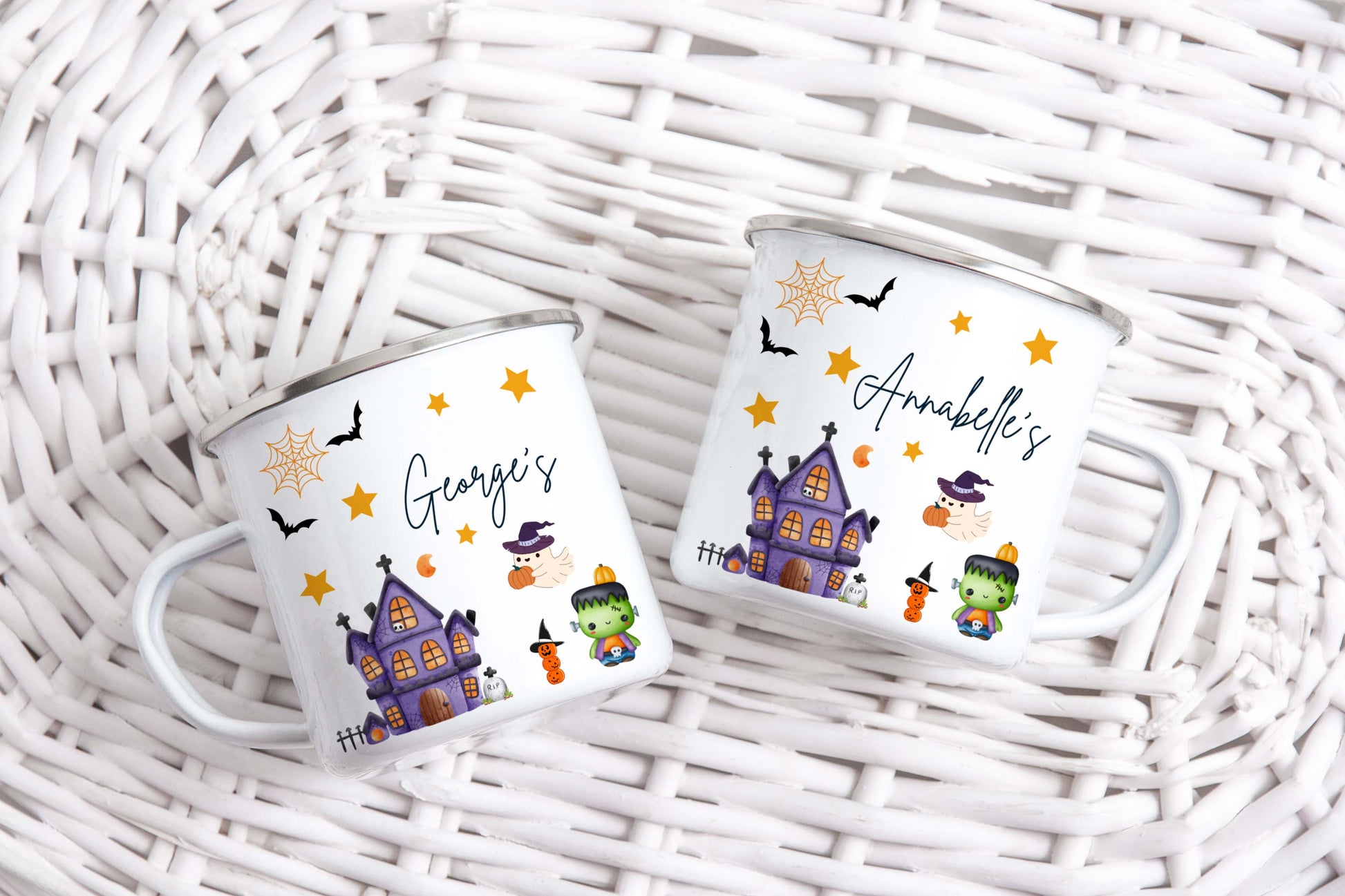 Two Halloween-themed enamel mugs with personalised names on a wicker surface