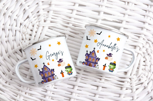 Two Halloween-themed enamel mugs with personalised names on a wicker surface