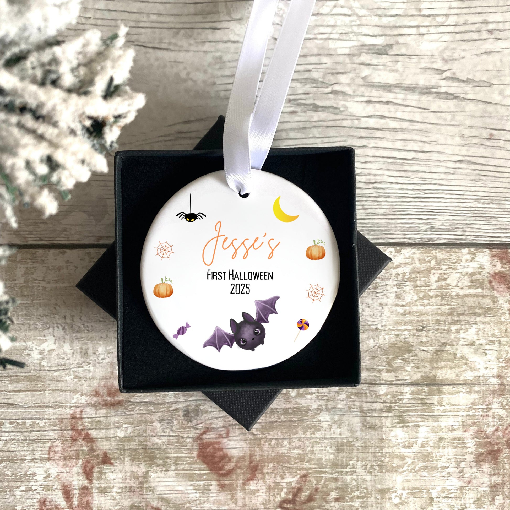 Personalised Halloween ornament for a child's first Halloween, featuring pumpkins, bats, and a moon, in a black box on a wooden surface.
