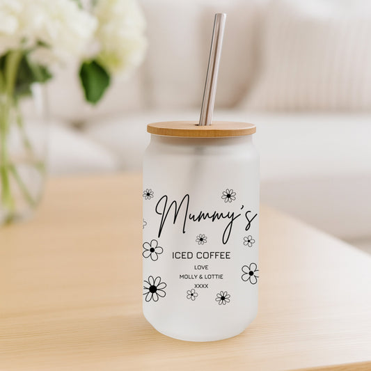 Glass tumbler with wooden lid and straw on a wooden surface with flowers in the background