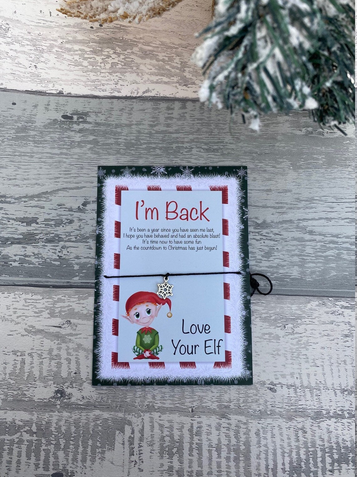 Card with text 'I'm Back' and 'Love Your Elf' on a wooden surface with a Christmas tree.