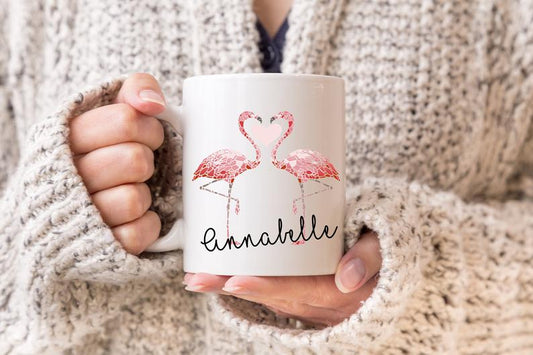 Person holding a personalised mug with flamingo design and 'Annabelle' text, wearing a cozy sweater.