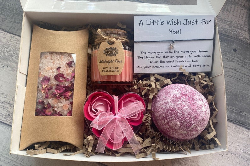 Gift box with bath products including a candle, bath bomb, and bath salts on a wooden surface.