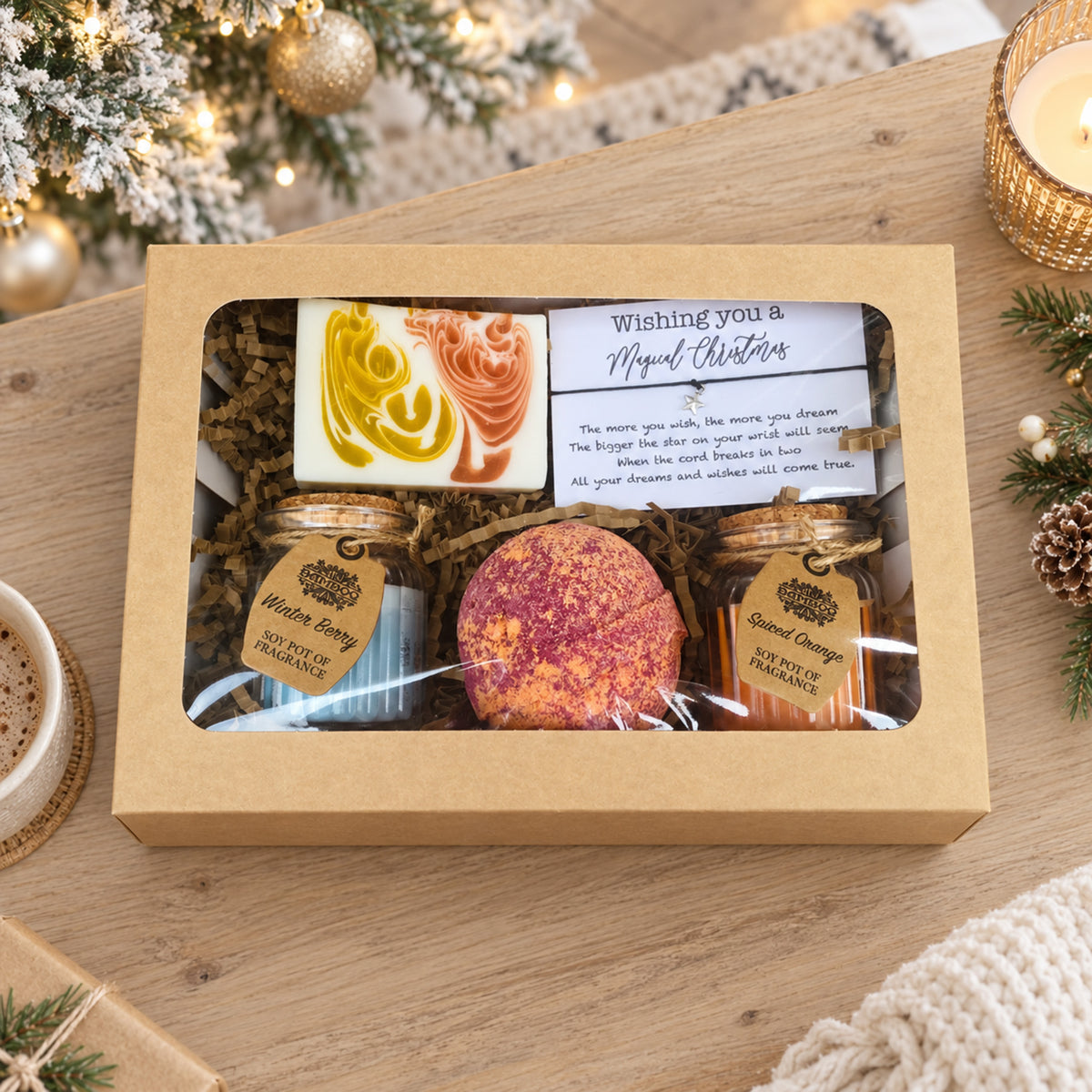 A holiday-themed gift box containing a marbled soap bar, two small candle bottles, and a magical christmas wish bracelet, displayed on a wooden table with festive decorations.