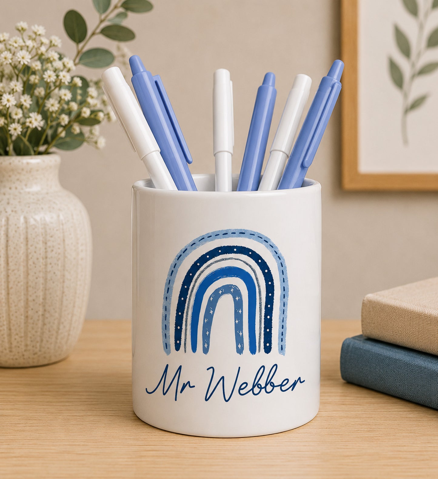 White teacher pencil pot with colourful rainbow design and custom name text, filled with pens on a wooden surface.