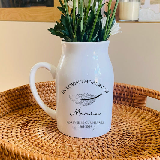 White memorial vase pitcher with floral arrangement on a woven tray, with 'In Loving Memory of Maria' text.