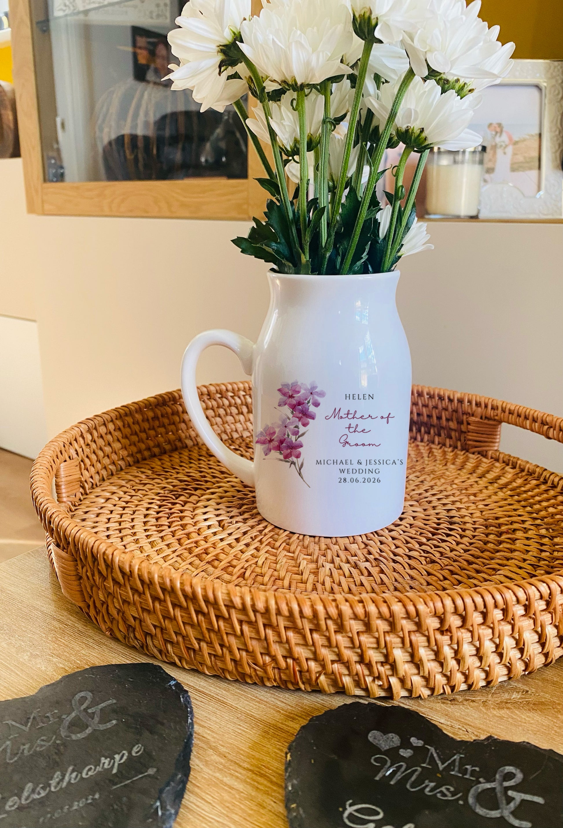 White pitcher with floral arrangement on a woven tray with 'Mr & Mrs' slate decorations.