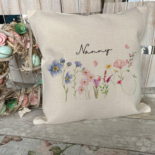 Decorative pillow with floral design and 'Nanny' text on a wooden surface.