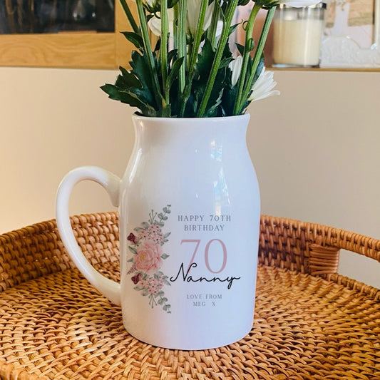 White 70th birthday vase pitcher with floral design on a woven tray
