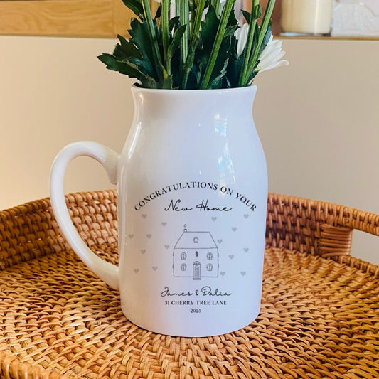 A personalised White pitcher vase with flowers on a woven tray in a home setting. The wording includes 'Congratulations on your new home'