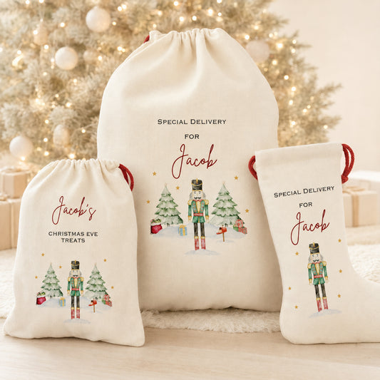 Three personalized cream-colored fabric drawstring gift bags with red handles, featuring nutcracker illustrations and text including 'SPECIAL DELIVERY FOR Jacob' and 'Jacob's CHRISTMAS EVE TREATS', arranged in front of a softly blurred decorated Christmas tree.