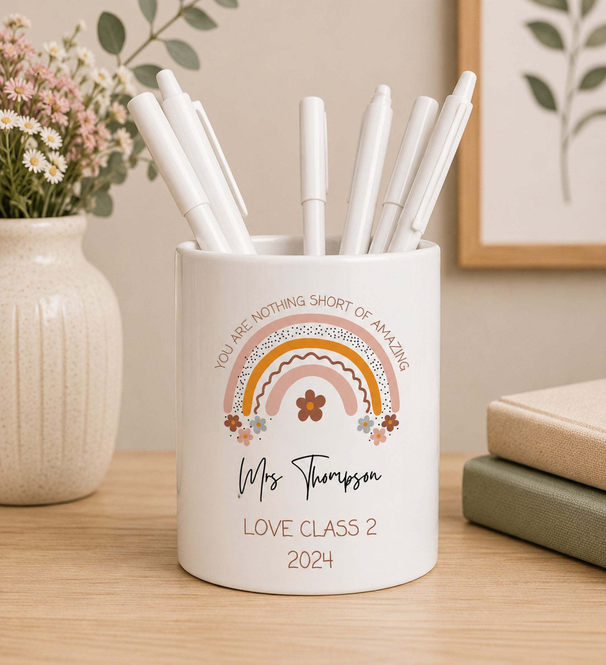 White teacher pencil pot with colourful rainbow design including the phrase 'You are nothing short of amazing' and custom name text, filled with pens on a wooden surface.