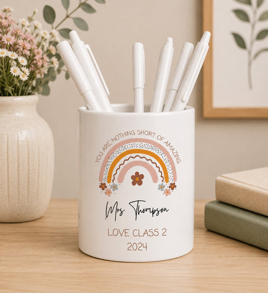 White teacher pencil pot with colourful rainbow design including the phrase 'You are nothing short of amazing' and custom name text, filled with pens on a wooden surface.