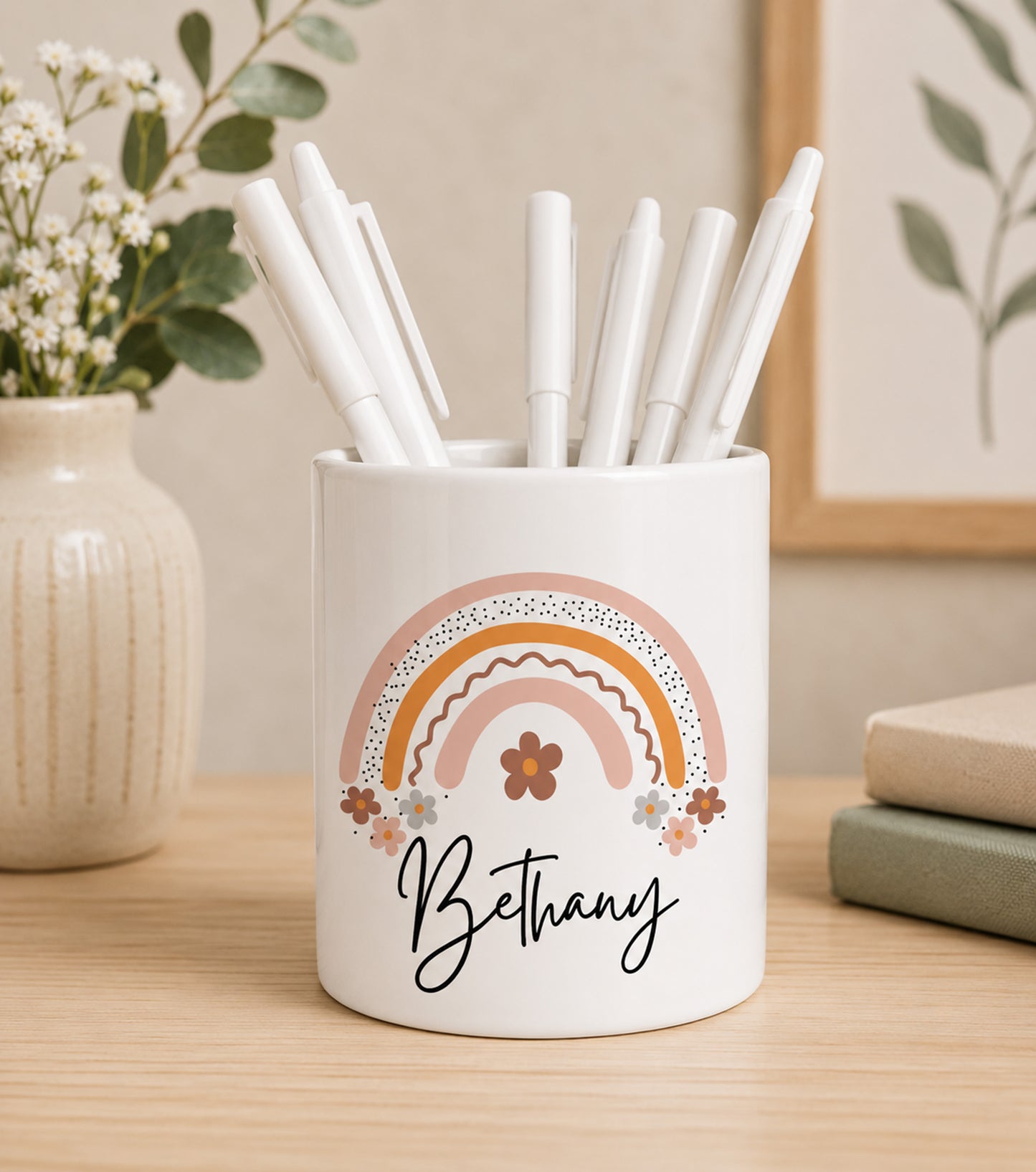 White teacher pencil pot with colourful rainbow design and custom name text, filled with pens on a wooden surface.