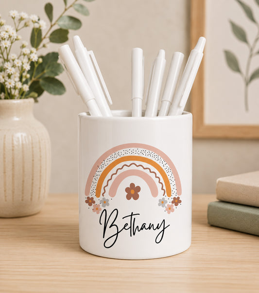 White teacher pencil pot with colourful rainbow design and custom name text, filled with pens on a wooden surface.