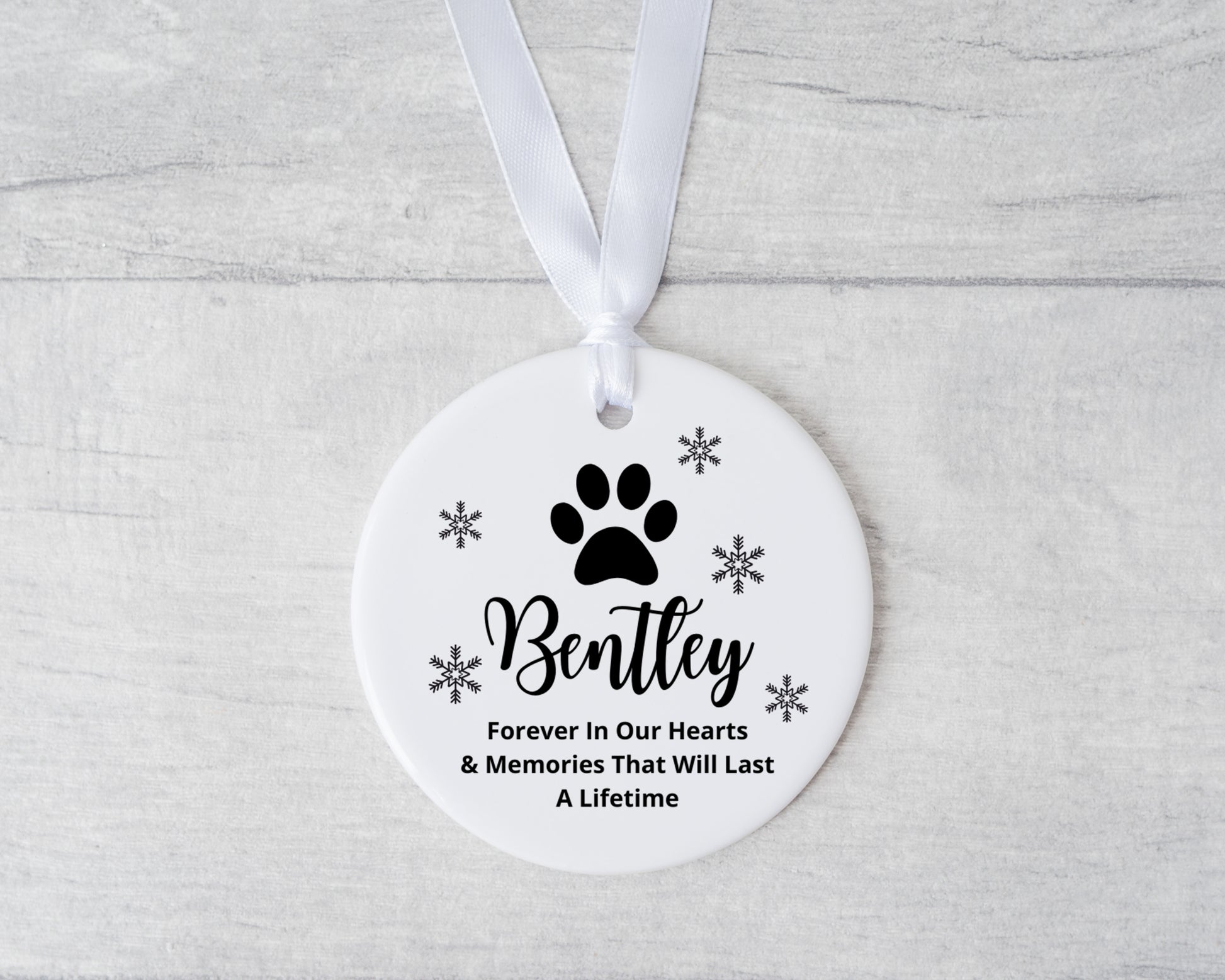 Round ceramic ornament with paw print and text on a white ribbon against a light gray background
