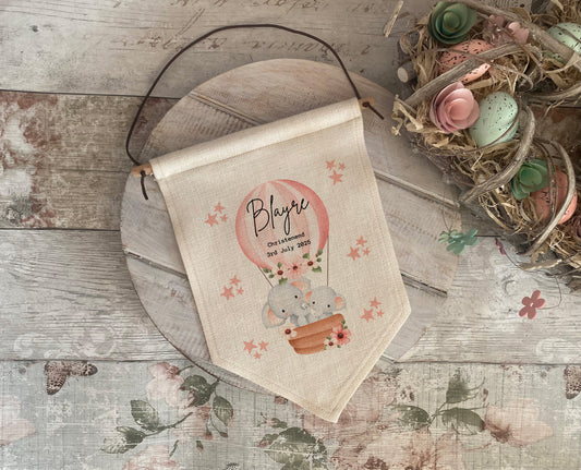 Decorative banner with a cartoon elephant in a hot air balloon on a wooden surface.