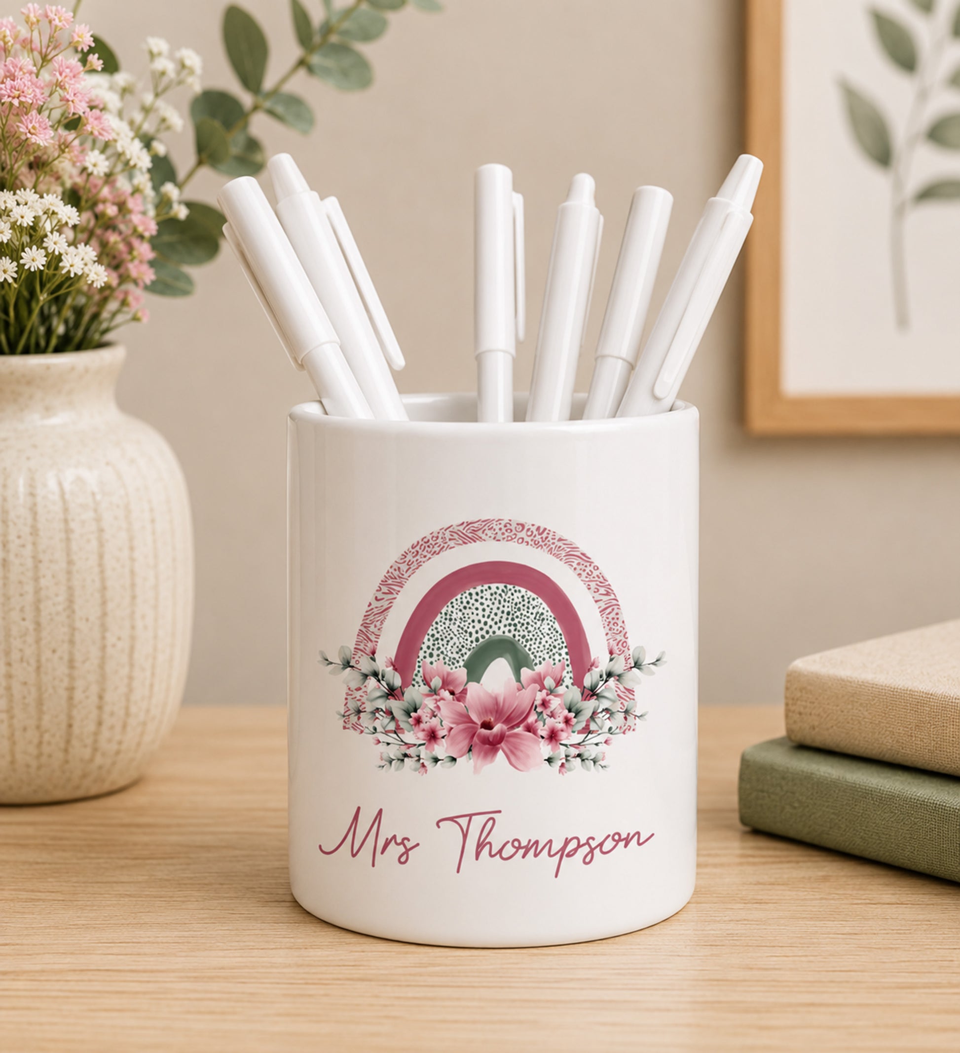 White teacher pencil pot with colourful rainbow design and custom name text, filled with pens on a wooden surface.