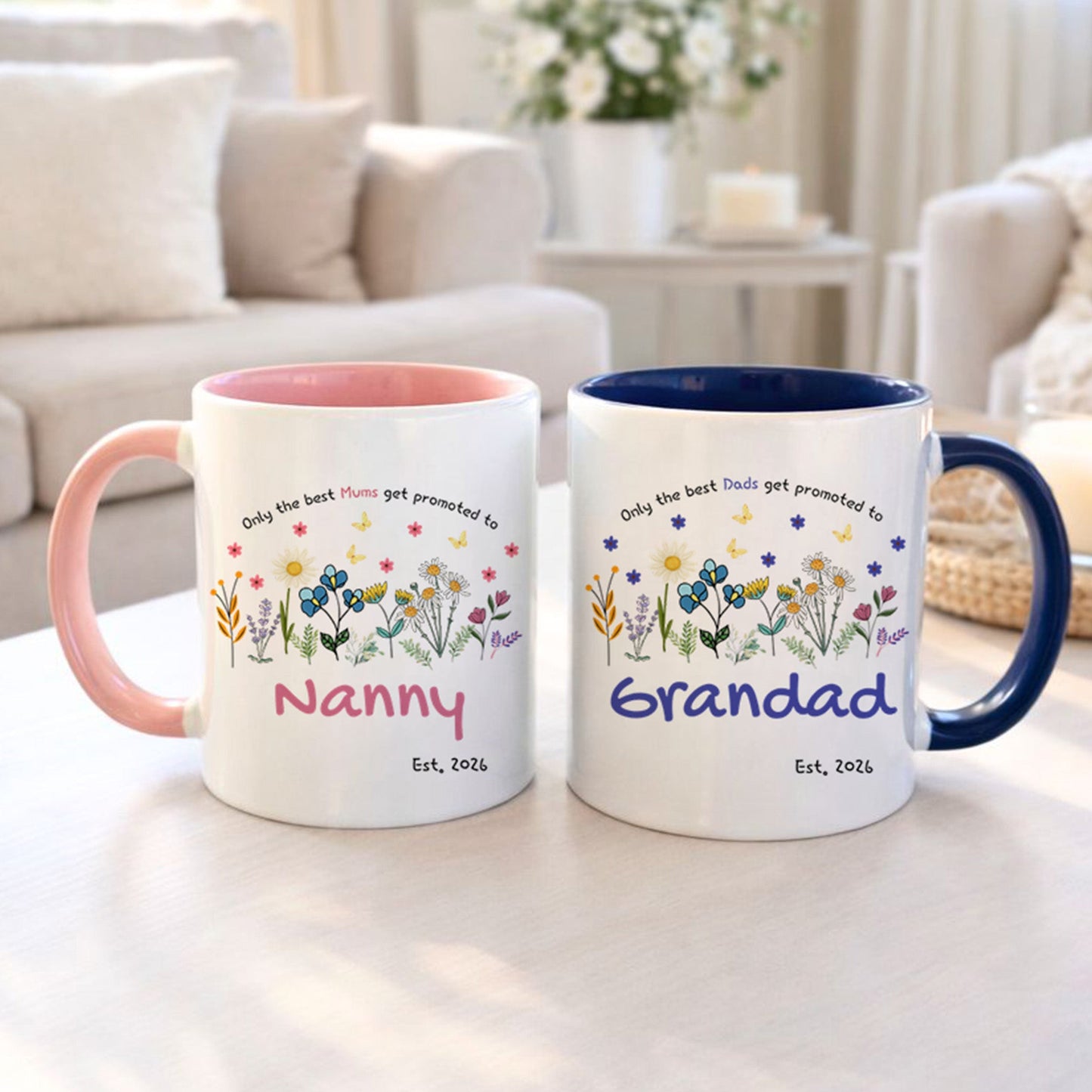 Two mugs with floral designs and text on a table in a living room setting.