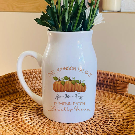 White pitcher with pumpkin design on a woven tray with flowers