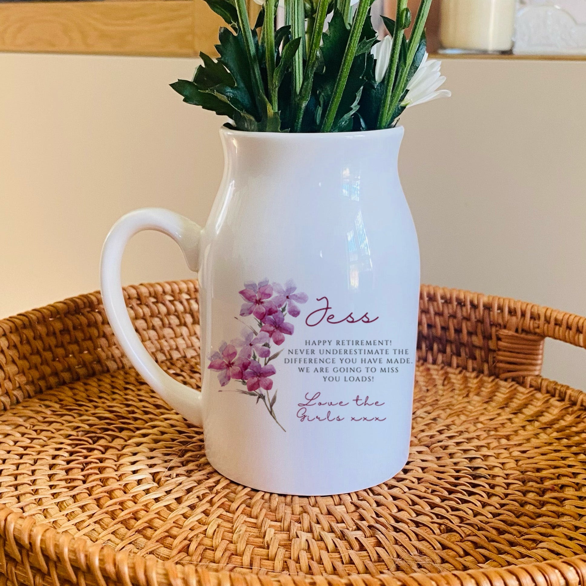 White pitcher with floral design on a wicker tray with flowers