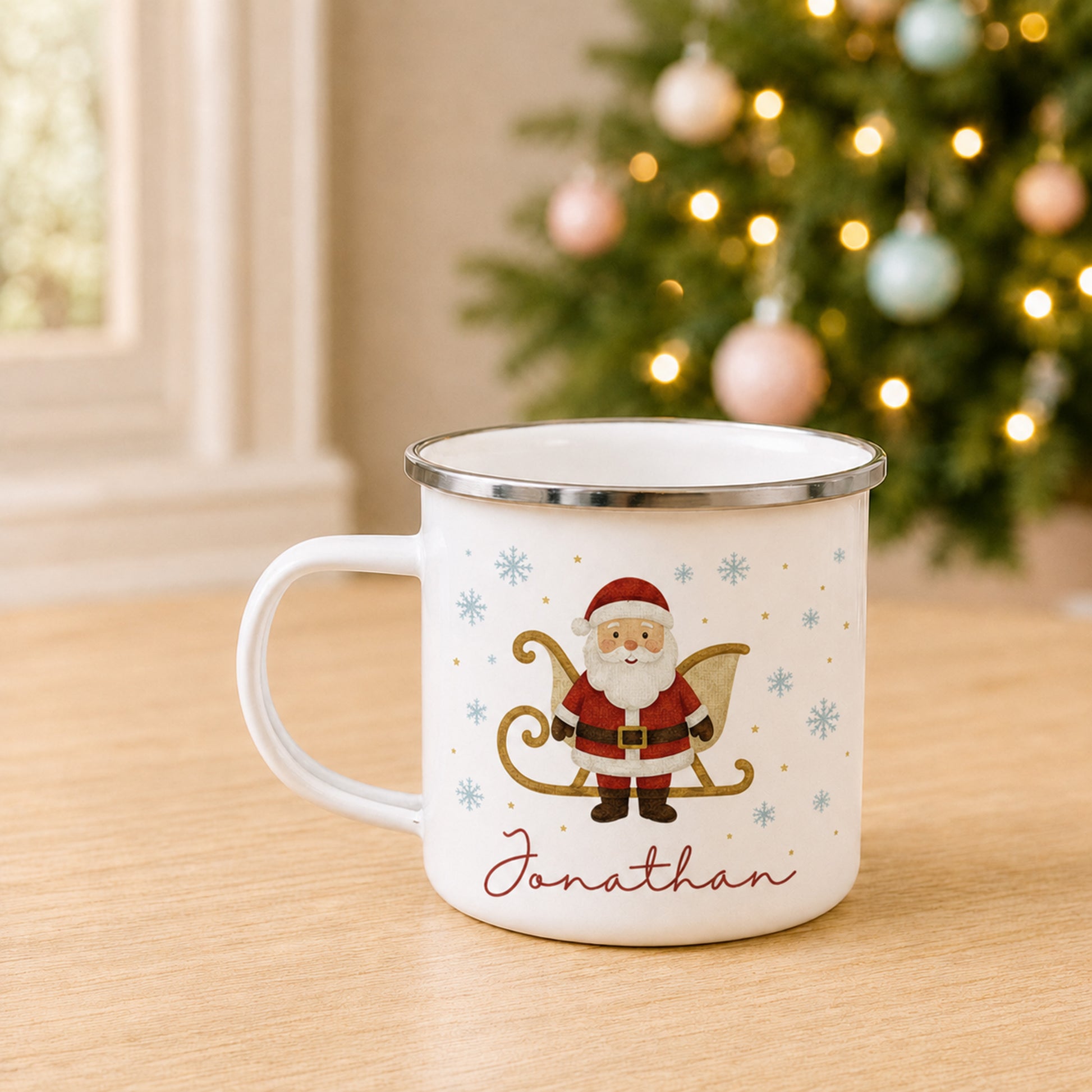A white enamel-style mug with a silver rim, featuring a Santa Claus illustration on a sled with snowflakes and the name 'Jonathan' in red script, set on a wooden table with a blurred Christmas tree in the background.