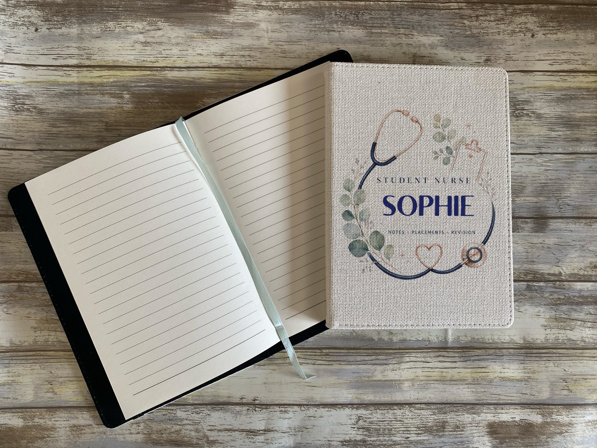 A personalized student nurse notebook shown open and closed on a rustic wooden background. The closed cover features a linen-textured design with a stethoscope, eucalyptus leaves, and the text 'STUDENT NURSE SOPHIE'.