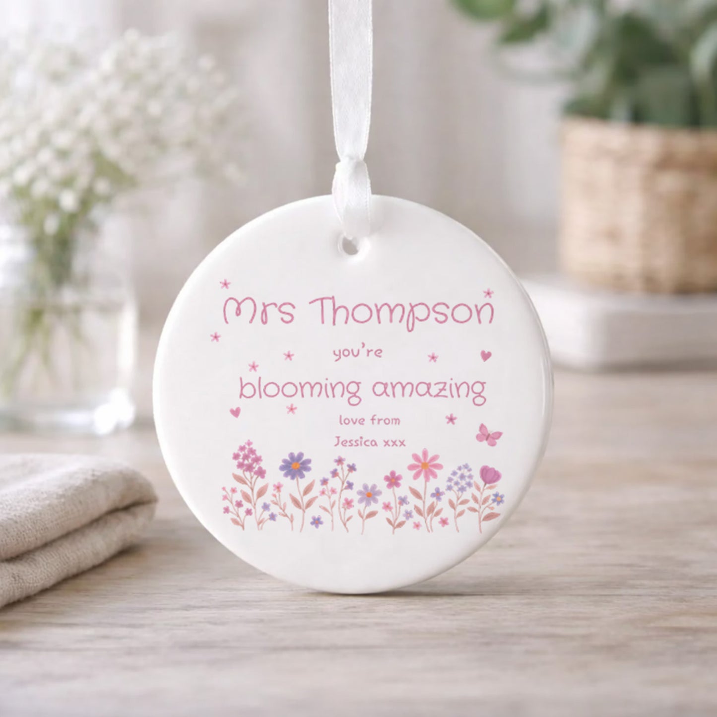 Round white ceramic ornament with floral design and text on a wooden surface.