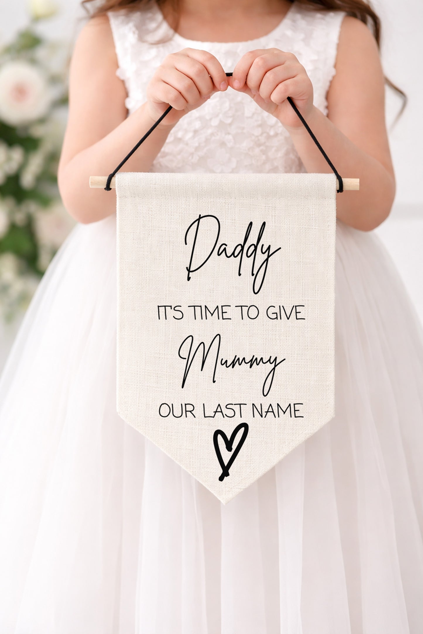 Child holding a sign with text in a white dress against a blurred floral background