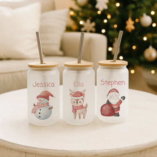 Three personalised Christmas-themed tumblers on a table with a decorated tree in the background.