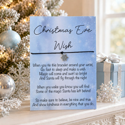 A Christmas-themed card with a message for 'Christmas Eve Wish' and a small bracelet across the center, styled on a mantel in front of a decorated Christmas tree and gift boxes.