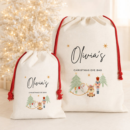 Two personalized cream Christmas Eve drawstring bags with red cords, one small and one large, printed with 'Olivia's Christmas Eve Bag' and festive illustrations, set against a warm, softly lit holiday background.