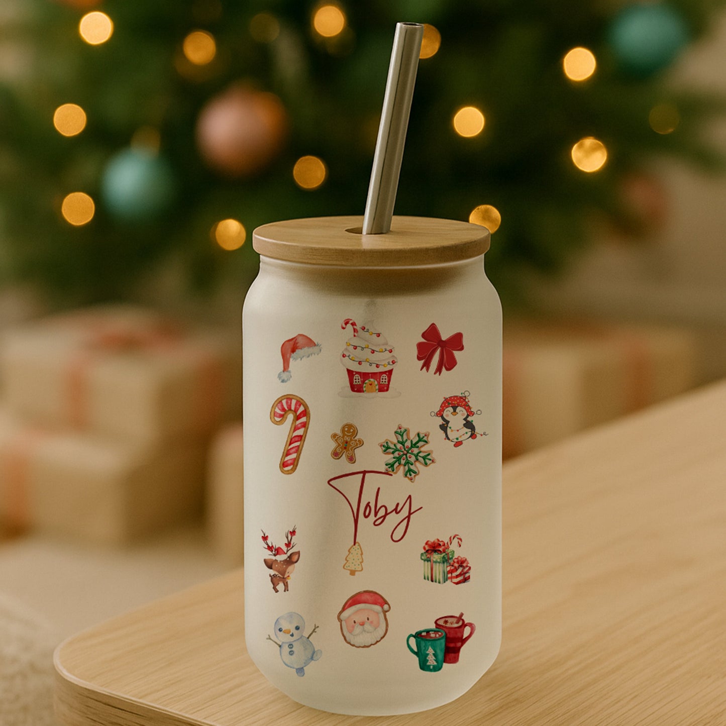 White tumbler with Christmas-themed illustrations on a wooden table in front of a decorated Christmas tree.