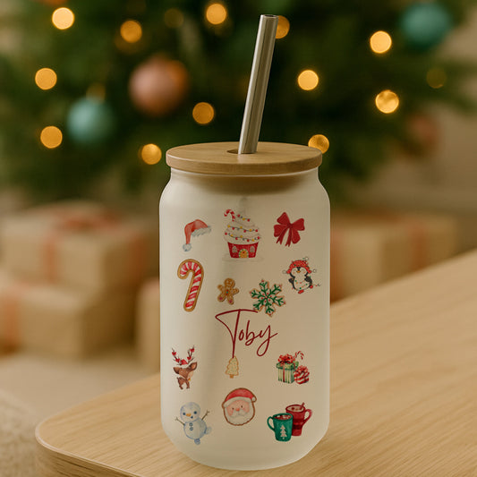 White tumbler with Christmas-themed illustrations on a wooden table in front of a decorated Christmas tree.